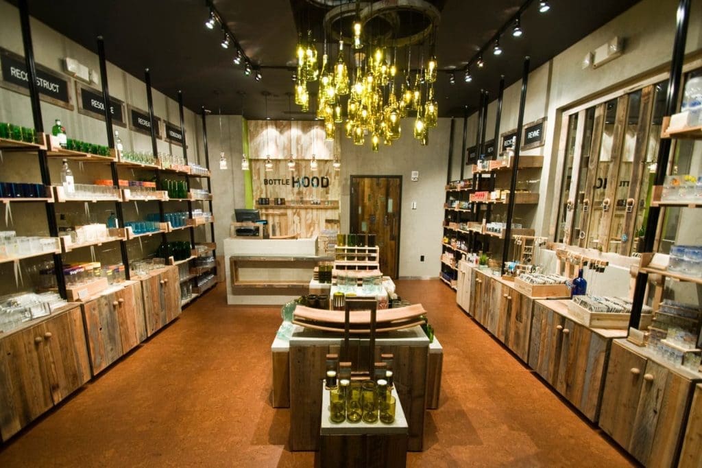 A well-lit shop interior with wooden shelves and tables displaying various bottles and glassware, under a modern chandelier with multiple hanging bulbs.