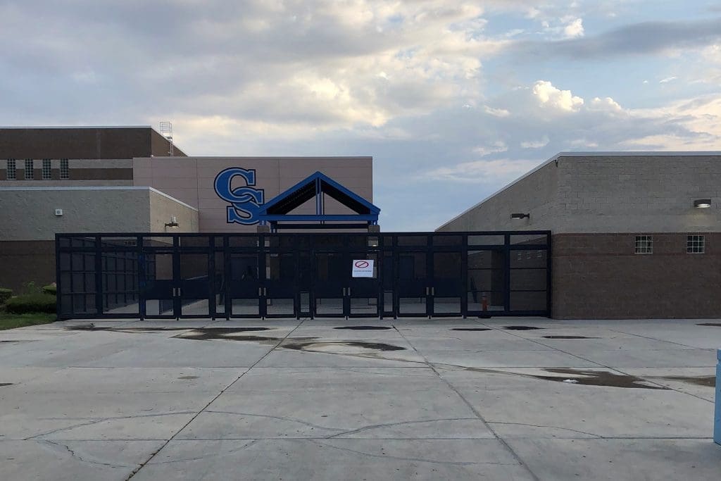 The entrance of a school building with large glass doors and a blue metal awning, featuring the letters "CS" on the wall above.