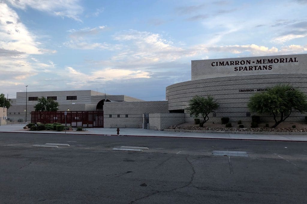 A wide view of the Cimarron-Memorial High School building with "Spartans" on the facade, surrounded by trees and a mostly empty street in front.