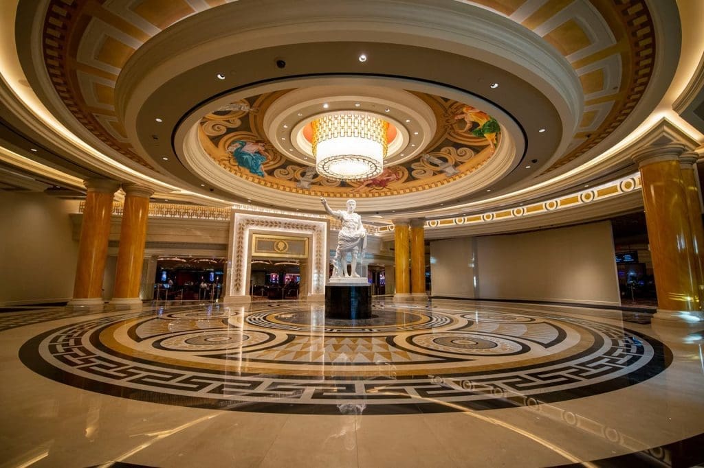 Spacious, ornate hotel lobby with a large circular ceiling, central statue, decorative columns, patterned floor, and a prominent chandelier.