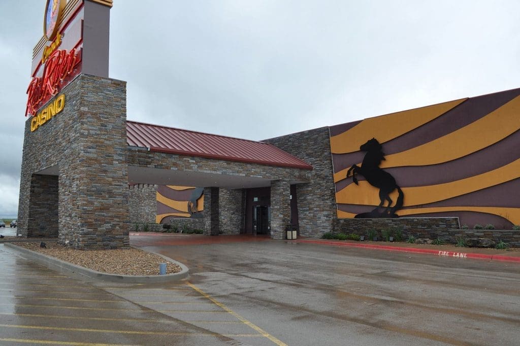 Exterior of a casino building with stone walls, a red metal roof, and a large black horse silhouette on a yellow and brown striped wall.