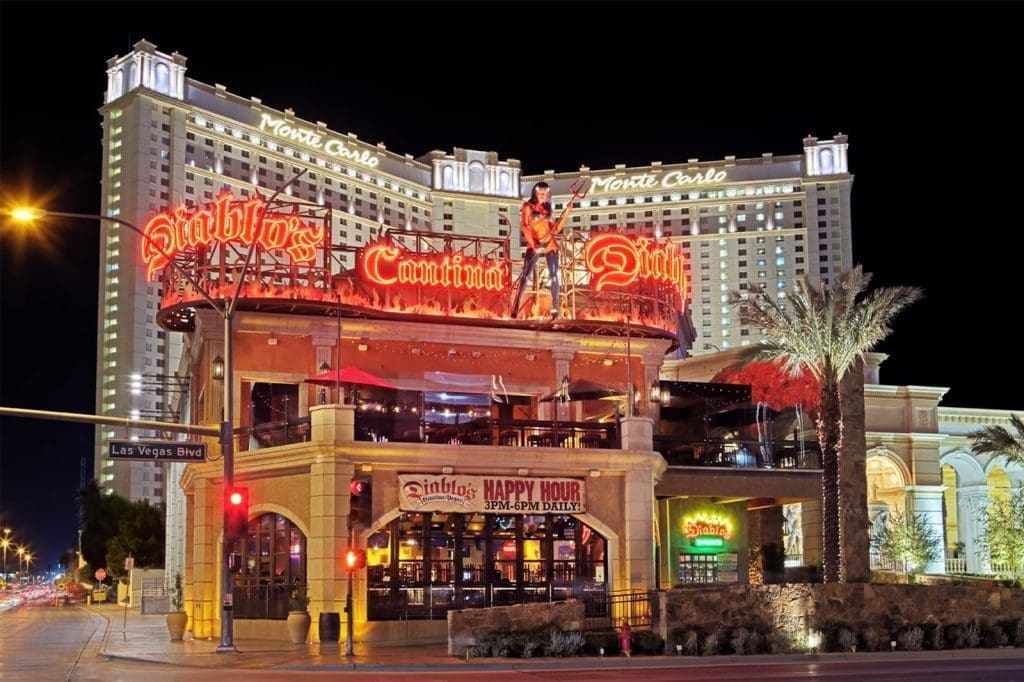Diablo's Cantina bar and restaurant with neon signs lit up at night, with the Monte Carlo hotel in the background on Las Vegas Boulevard.