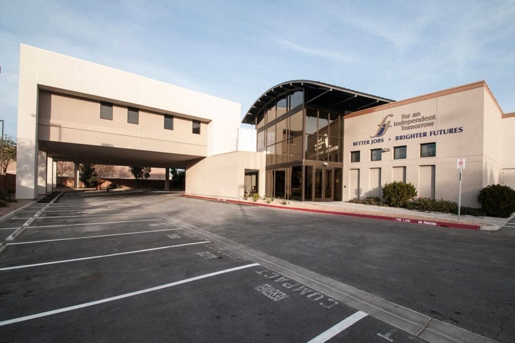 Modern office building with large glass entrance and a drive-through section; logo and slogan "Better Jobs. Brighter Futures." visible on the facade; empty parking lot in front.
