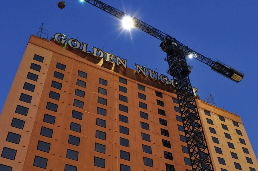 A construction crane is positioned next to the Golden Nugget hotel building at dusk, with its name displayed in large letters on the upper facade.