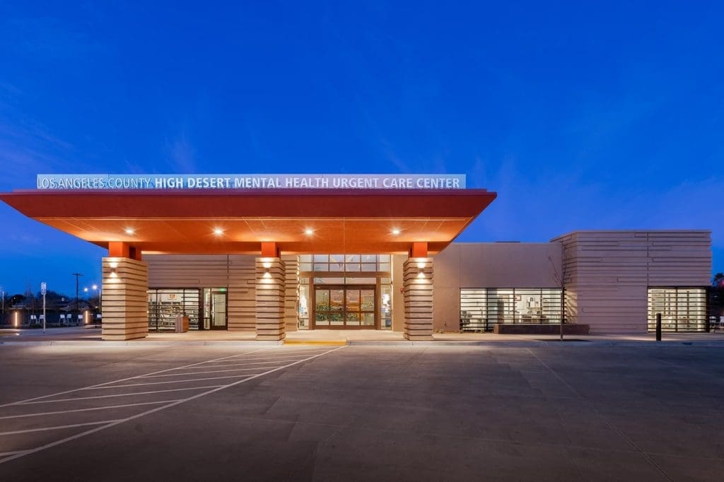 Exterior view of the Los Angeles County High Desert Mental Health Urgent Care Center at dusk, with illuminated signage and modern architecture.