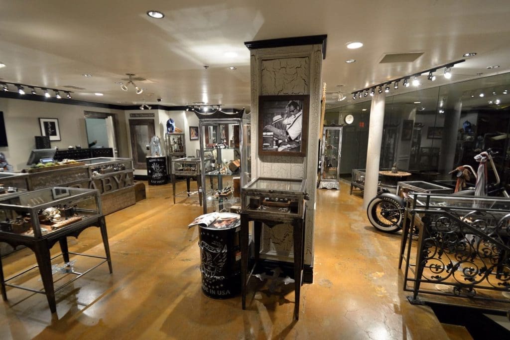 A motorcycle-themed showroom with display cases, framed photos on the walls, and a motorcycle partially visible on the right side. The floor is polished and the lighting is bright.