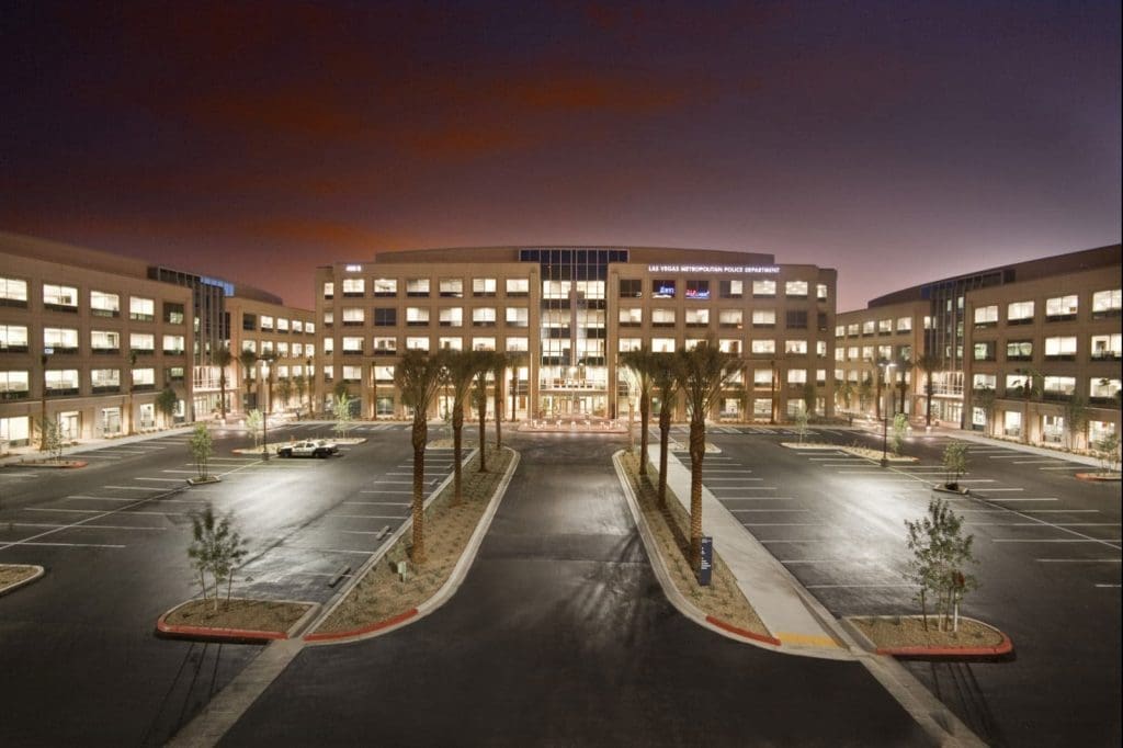Large modern office building with three wings, palm trees lining the entrance, and an empty parking lot at dusk.