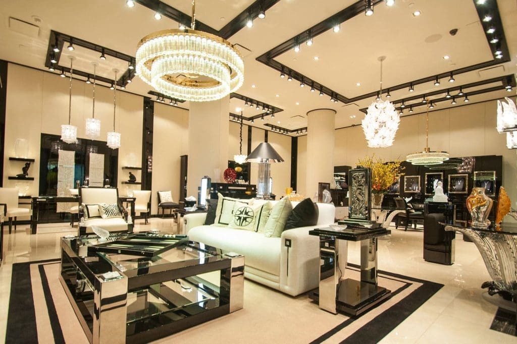 A modern luxury furniture showroom with chandeliers, glass tables, sofas, and decorative items displayed under bright lighting.