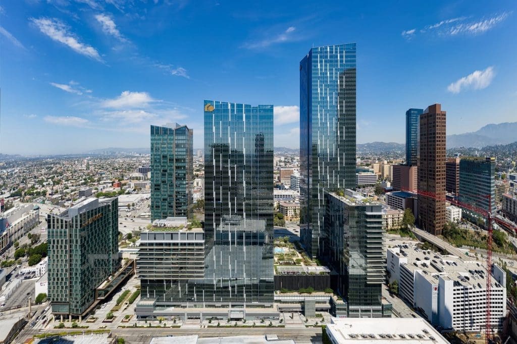 Aerial view of modern high-rise office buildings in a downtown urban area with clear skies and mountains in the background.