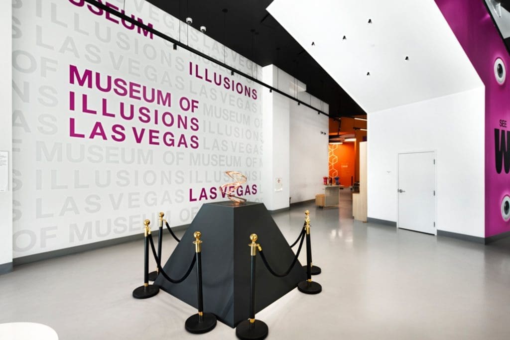 Interior of the Museum of Illusions in Las Vegas featuring a black display pedestal with a basketball enclosed by stanchions, and museum signage on white walls.