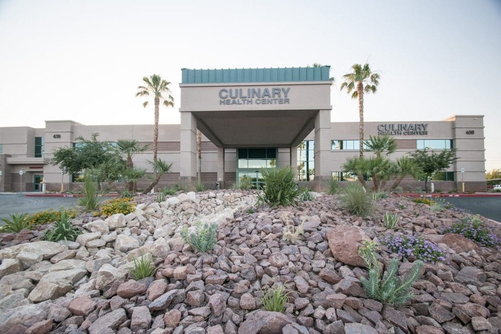 Front view of the Culinary Health Center building with landscaped rocks, desert plants, and palm trees in the foreground.