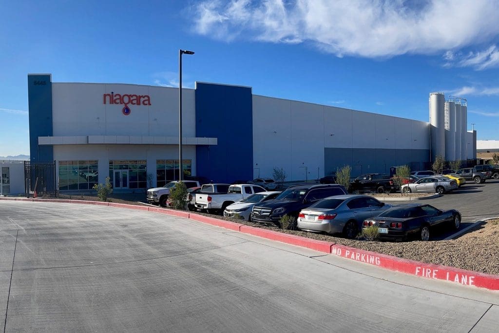 A large industrial building with a "niagara" sign, several parked cars in the lot, and visible water tanks in the background under a blue sky.