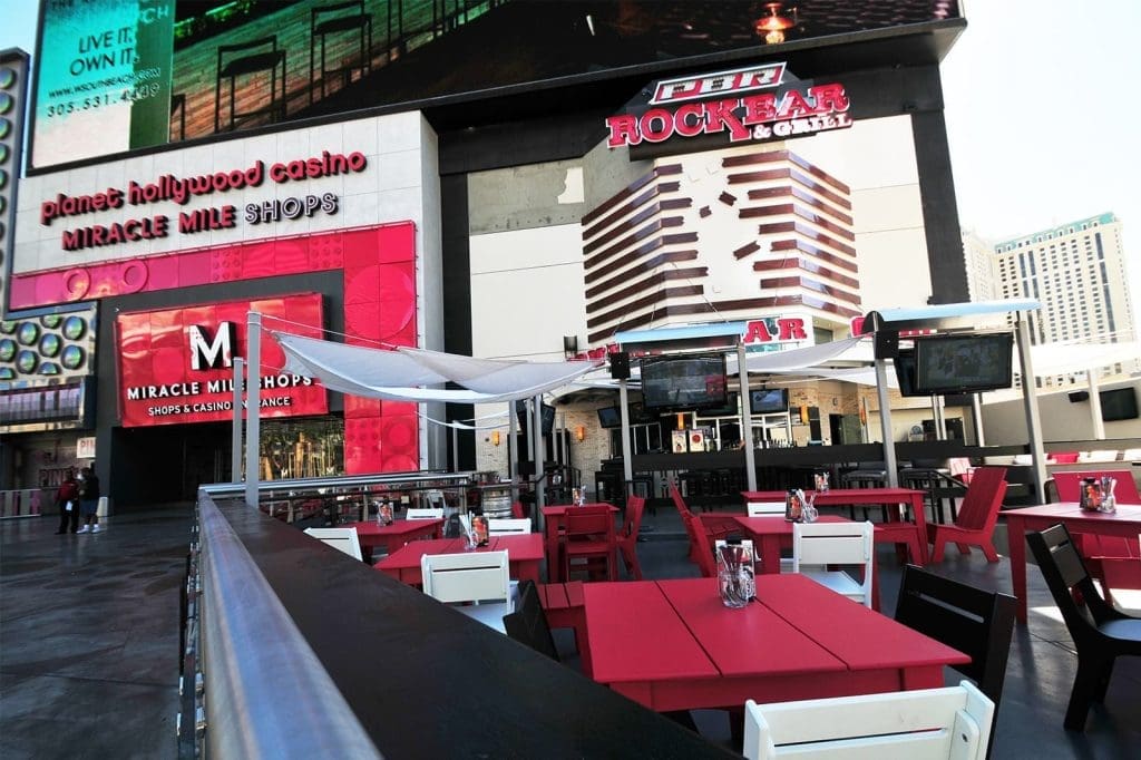 Outdoor dining area with red and white tables and chairs in front of PBR Rock Bar & Grill, located near Miracle Mile Shops and Planet Hollywood Casino.