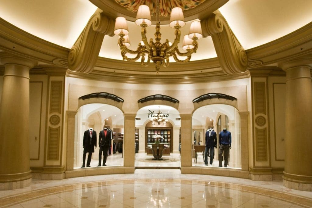 A chandelier-lit hallway leads to a formal menswear store with mannequins in suits and shirts displayed in the windows.