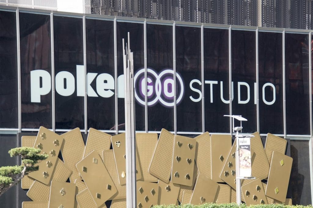 The exterior of a building with large windows displays the "PokerGO Studio" logo above a decorative wall featuring oversized gold playing cards.