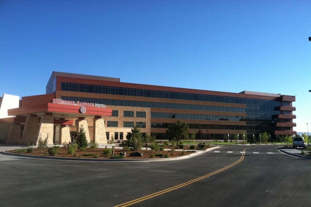Modern multi-story building with large windows and a sign reading "Snoqualmie Ballroom Hotel" at the entrance, surrounded by landscaping under a clear blue sky.