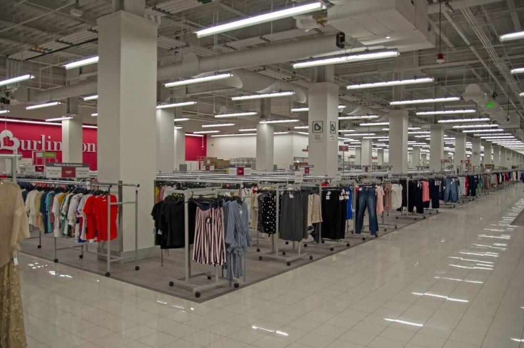 Interior of a brightly lit retail clothing store with racks of assorted clothes and tiled floors.