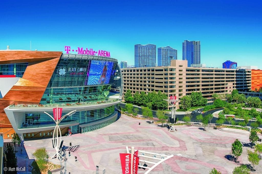 T-Mobile Arena is shown next to a multi-story parking garage and landscaped plaza constructed by PENTA on a clear, sunny day with tall buildings in the background.