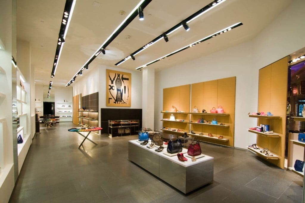 A modern boutique store interior displays handbags, shoes, and accessories on shelves and tables, with bright lighting and minimalist décor.