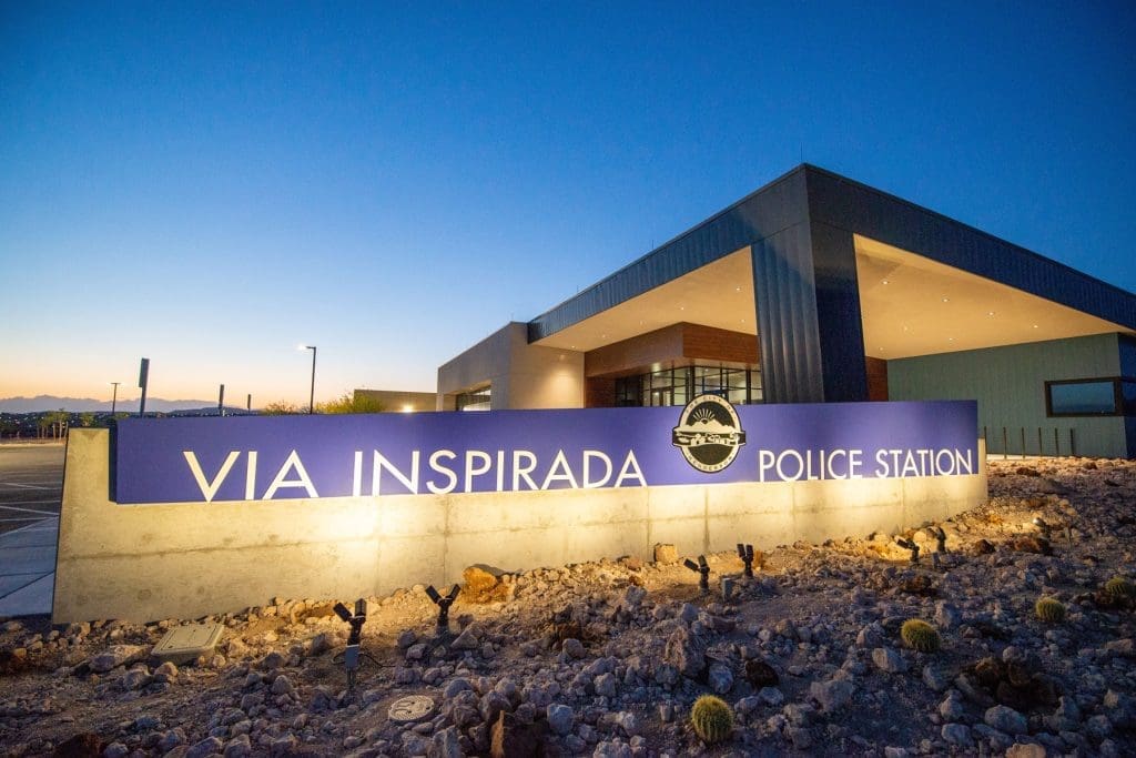 A modern building with a sign reading "Via Inspirada Police Station" illuminated at dusk, with desert landscaping in the foreground.