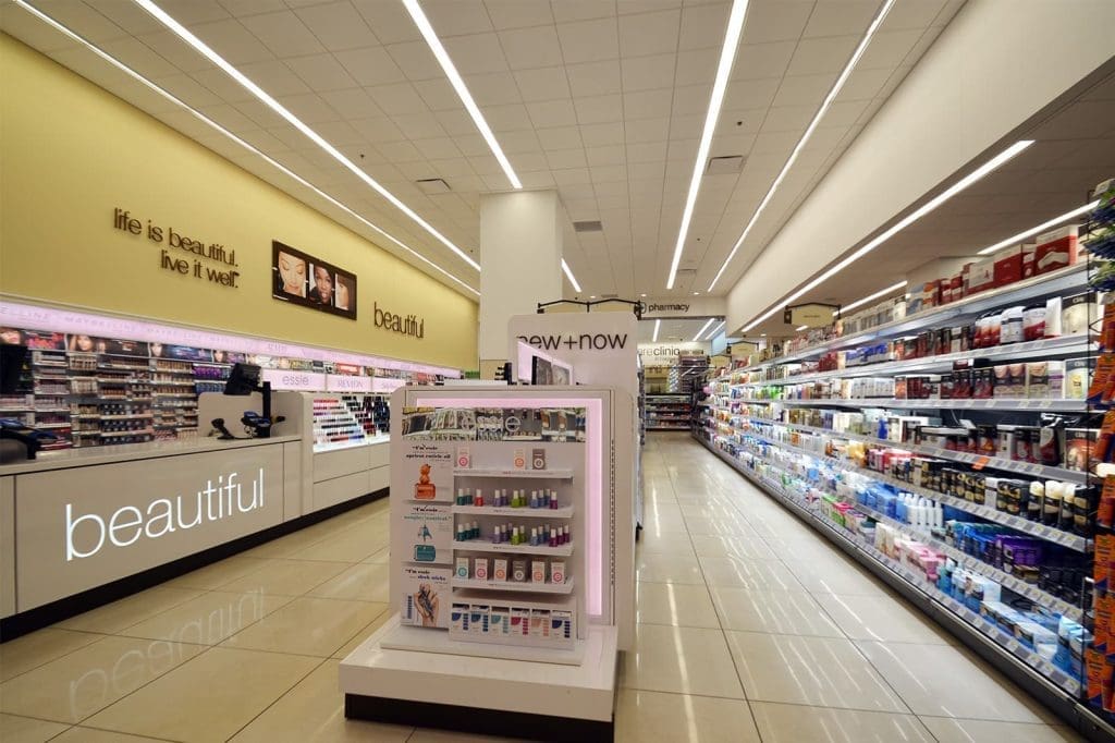 A brightly lit drugstore beauty aisle with skincare and cosmetic displays, shelves of products, and signage reading "beautiful" and "life is beautiful. live it well.
