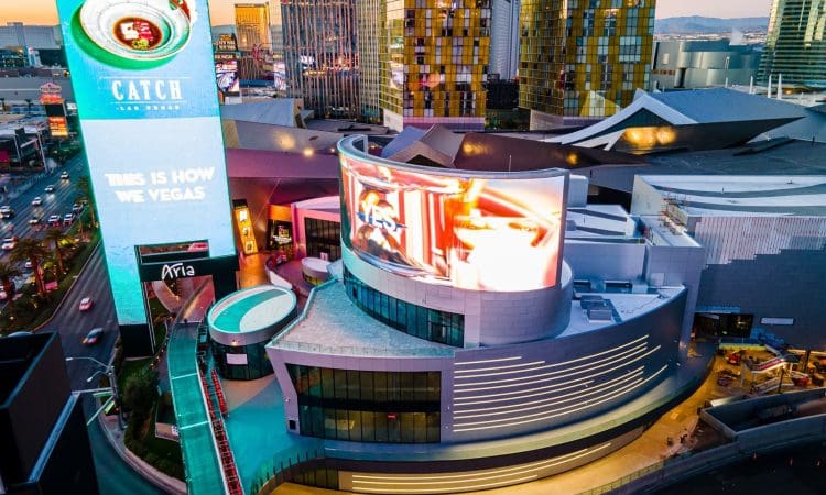 Aerial view of a modern commercial building in Las Vegas with large digital billboards displaying colorful advertisements at dusk.