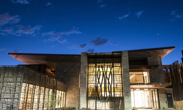 Modern building with large glass windows and unique architectural features, illuminated at night against a deep blue sky.