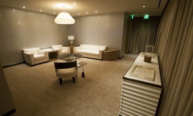 A modern, softly lit lounge with beige walls, a sofa, two armchairs, a side table, a lamp, and a console table along one wall.