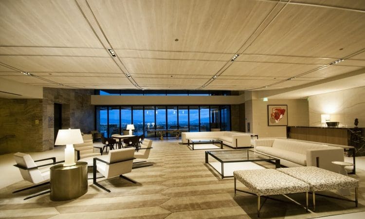 Spacious, modern hotel lobby with white sofas, armchairs, coffee tables, and large windows overlooking an outdoor view at dusk.