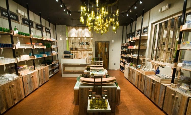 A well-lit shop interior with wooden shelves and tables displaying various bottles and glassware, under a modern chandelier with multiple hanging bulbs.