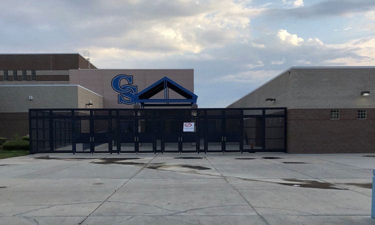The entrance of a school building with large glass doors and a blue metal awning, featuring the letters "CS" on the wall above.