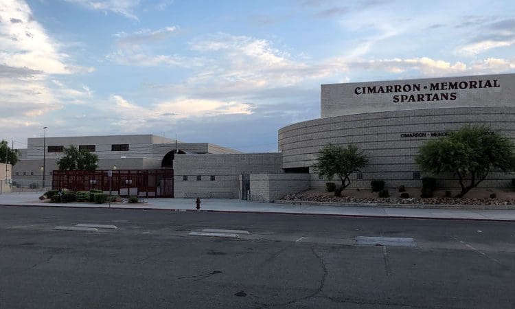 A wide view of the Cimarron-Memorial High School building with "Spartans" on the facade, surrounded by trees and a mostly empty street in front.