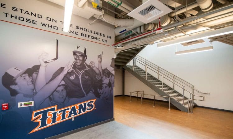 A wall mural of celebrating baseball players and the Titans logo in a modern hallway with a staircase and exposed ceiling pipes.