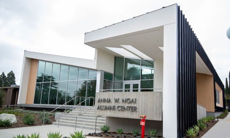 A modern building with large windows and a sign reading "Anna W. Ngai Alumni Center" above the entrance, surrounded by landscaped plants.