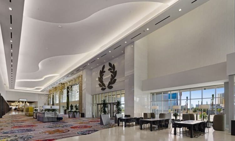 Spacious modern lobby with high ceilings, patterned carpet, lounge seating, large windows, and decorative wall art featuring a laurel wreath.