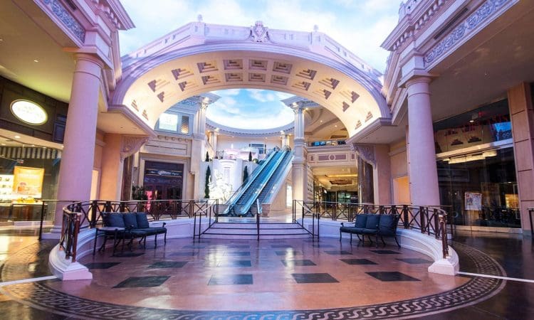 A spacious indoor shopping mall with classical architecture, an arched ceiling, central escalators, and decorative columns.