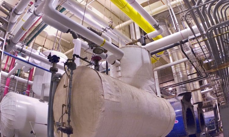 Industrial mechanical room with insulated pipes, large cylindrical tanks, gauges, and valves, used for heating or cooling systems.