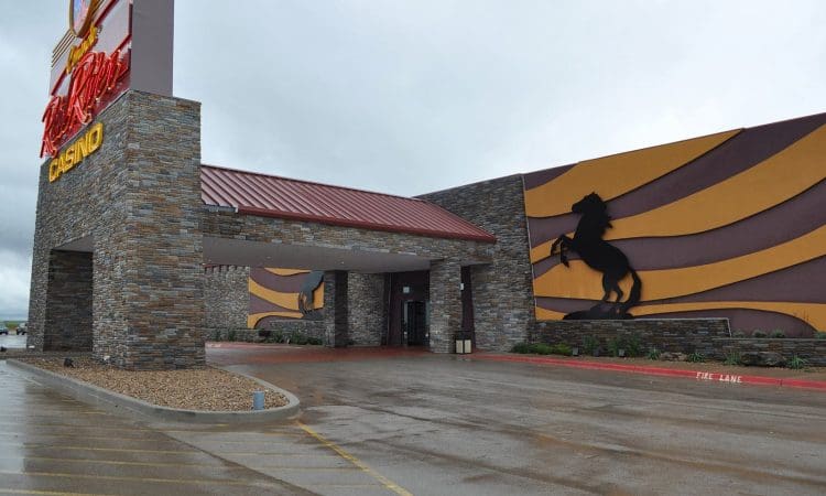 Exterior of a casino building with stone walls, a red metal roof, and a large black horse silhouette on a yellow and brown striped wall.