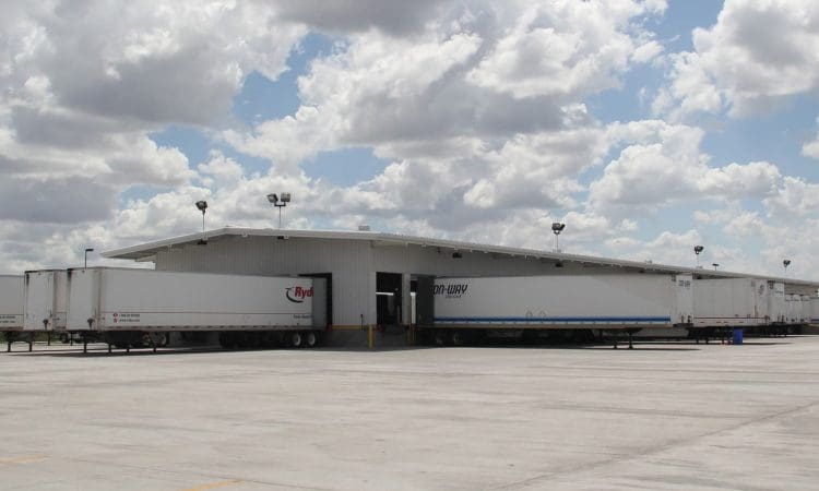 A large warehouse with multiple semi-trailers parked at loading docks under a partly cloudy sky.
