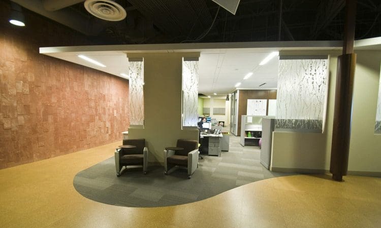 Modern office reception area with two chairs, decorative glass dividers, computers, and curved flooring design under ceiling ductwork.