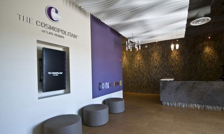 Lobby area of The Cosmopolitan of Las Vegas with a purple accent wall, round gray seats, a digital display, and a modern reception desk.