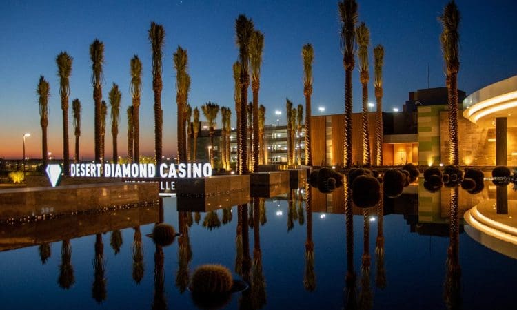 Desert Diamond Casino entrance at dusk, with palm trees and building lights reflected in a large pool of water.