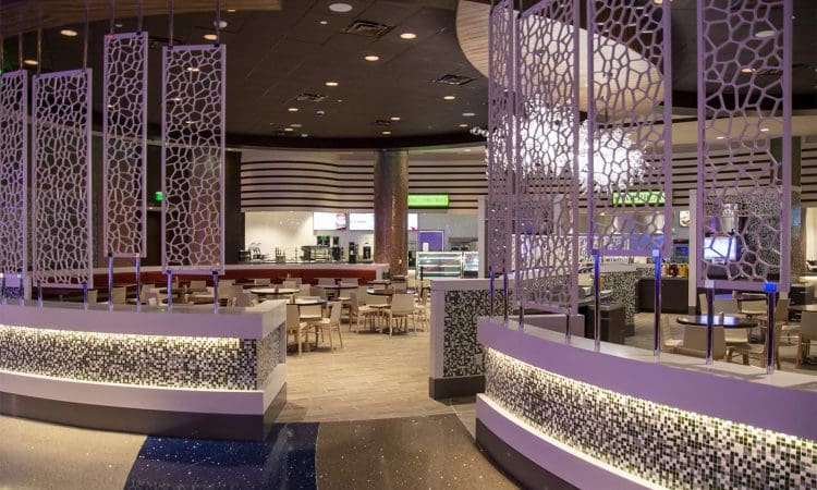 Modern dining area with geometric decorative partitions, mosaic tile accents, tables and chairs, and food counters in the background under ambient lighting.
