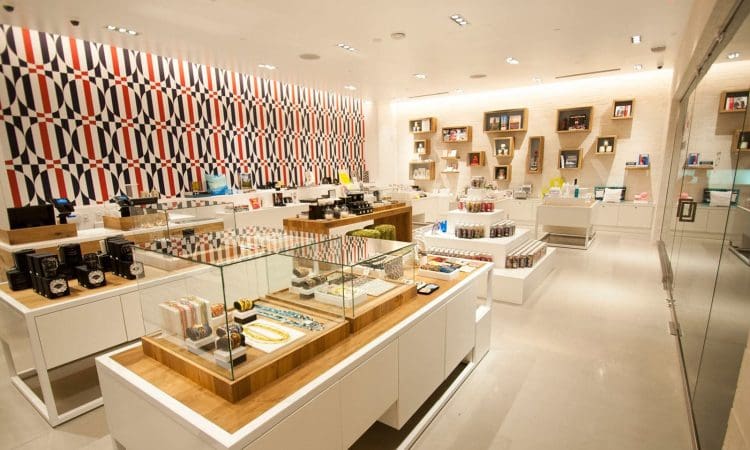 Modern retail store interior with well-lit displays of various products, glass cases, white shelves, and a geometric patterned accent wall.