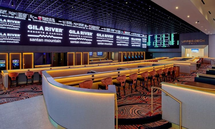 Modern casino sports betting area with rows of seating, individual screens, and large digital displays showing game information and odds.