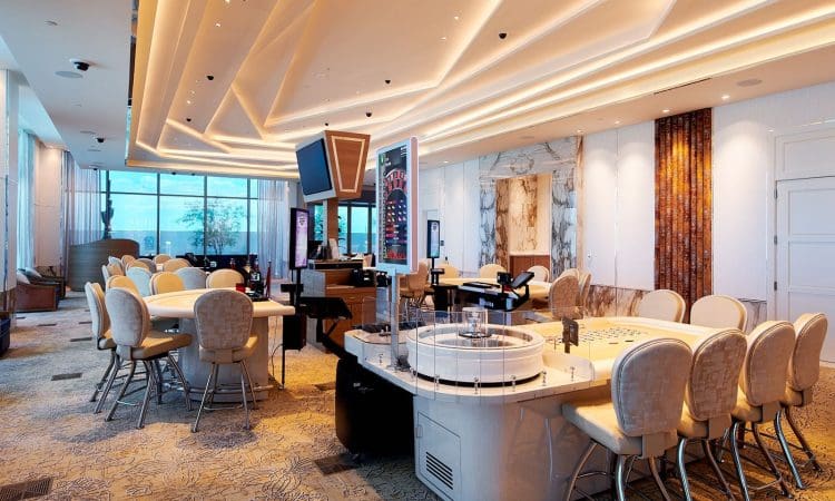 A modern, well-lit casino floor with gaming tables, slot machines, plush chairs, and large windows offering views outside.