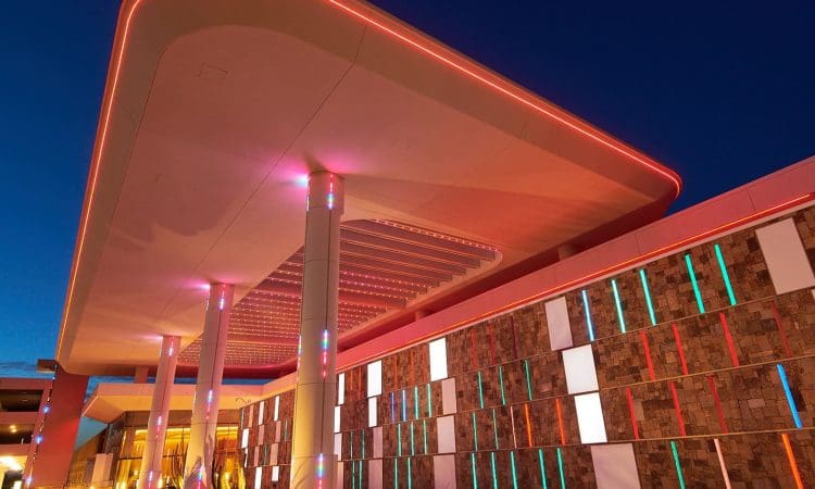 Modern building exterior at night with illuminated red and blue accent lights, featuring columns and a geometric patterned wall.
