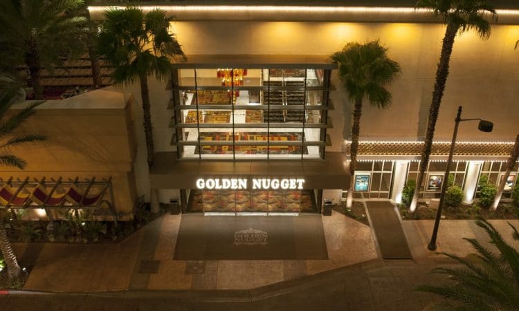 A nighttime view of the entrance to the Golden Nugget casino, with illuminated signage, glass windows, and palm trees lining the walkway.