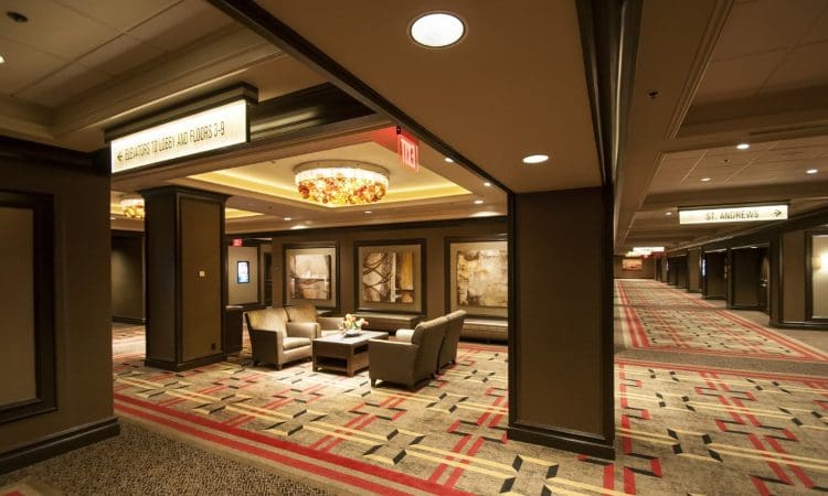Hotel hallway with patterned carpet, modern furniture, abstract wall art, and overhead lighting; conference room signs are visible.