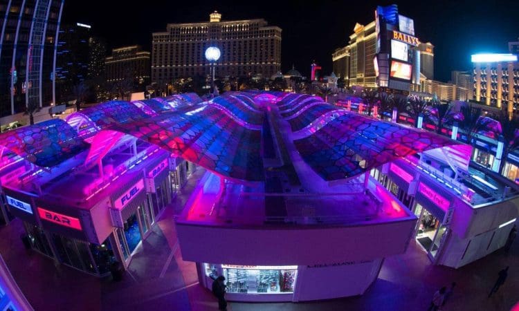 Night view of a shopping area with illuminated, colorful canopies and signs, with hotels and casinos in the background on the Las Vegas Strip.